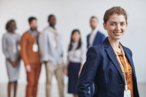 A young business professional looking confident with her colleagues in the background.