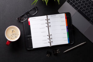 Top view of a notebook, a laptop, a pair of glasses, and a cup of coffee