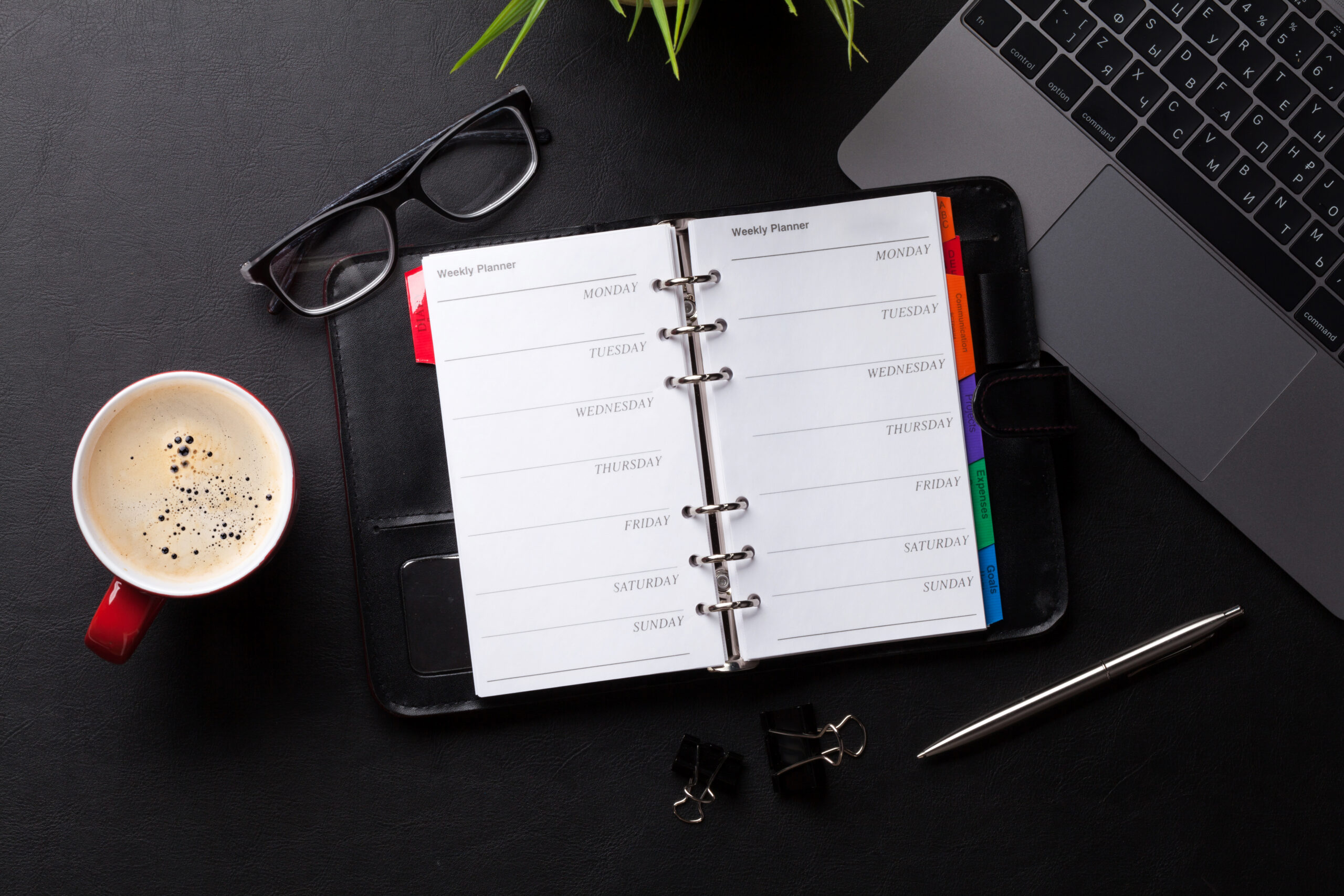 Top view of a notebook, a laptop, a pair of glasses, and a cup of coffee